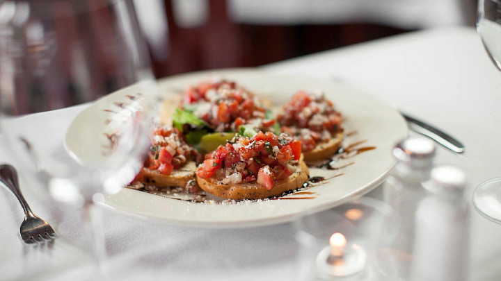 Plate of tomato bruschetta on white tablecloth with silverware, salt and pepper shakers