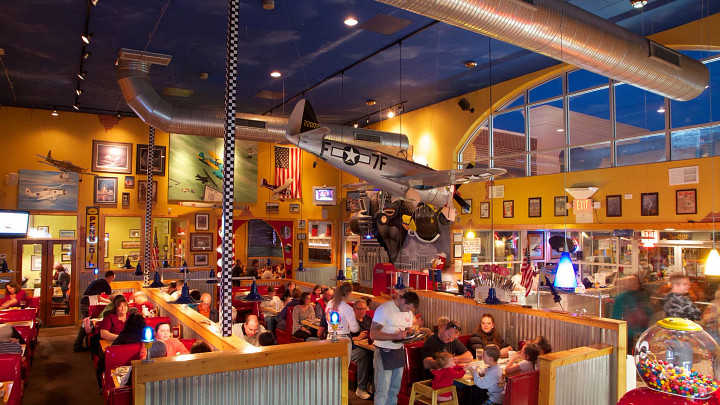 People seated in booths inside restaurant ordering food with airplanes overhead