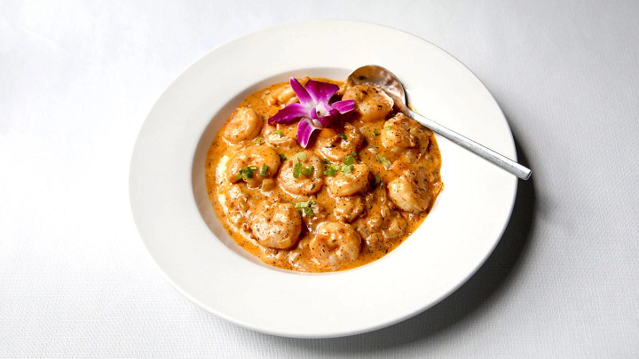 Bowl of shrimp and grits with gravy and spoon and flower garnish
