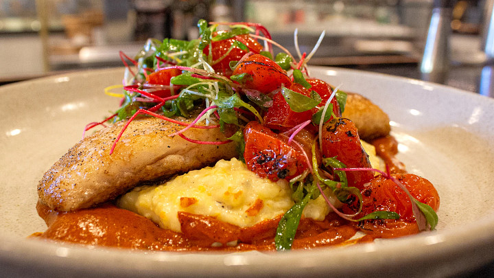 Fish, grits and vegetables on plate in restaurant