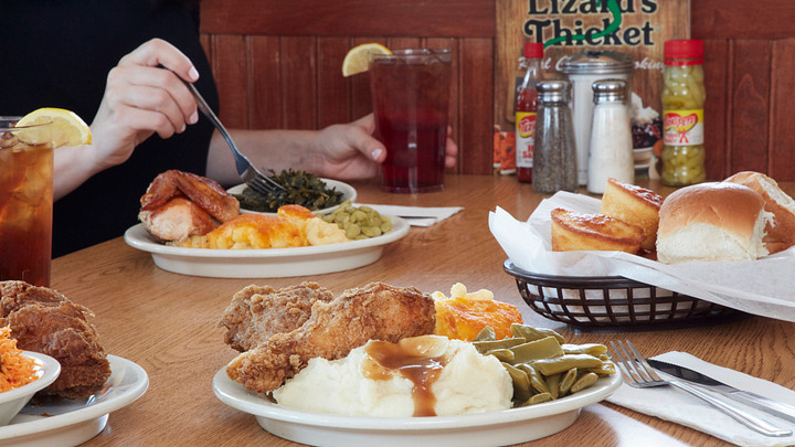 Table laden with plates of fried chicken, vegetables, tea, corn muffins